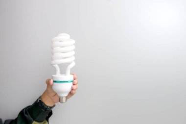 Enerji verimliliğini, yeniliği, sürdürülebilirliği ve parlak fikirleri temsil eden sarmal floresan ampulü (CFL) tutan bir elin minimalist konsept görüntüsü