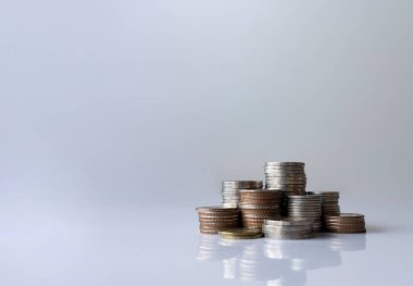 Temiz beyaz bir yüzey üzerinde düzenli olarak düzenlenmiş gümüş, bronz ve altın tonlardaki çeşitli madeni para yığınları finans, tasarruf ve yatırımı sembolize eder..