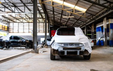 Araba tamirhanesinde boya ya da kaportayı kısmen kapatan bir araba tamir ediliyor.