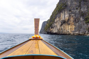 Tahta kuyruklu Tayland teknesi mavi okyanustaki uçurum kenarındaki adaya doğru gidiyor. Güneydoğu Asya 'da macera, seyahat ve tropikal deniz manzarasını gösteriyor.