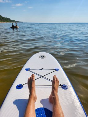 Sakin bir gölde, temiz mavi suyu ve sahilde yeşil ağaçları olan bir kürek tahtasında yatan biri. Huzurlu ve rahatlatıcı bir atmosfer yaratıyor. Yaz tatili için mükemmel..