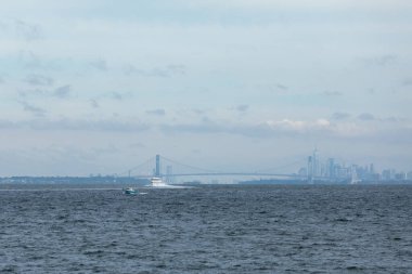 Belford, New Jersey - 30 Eylül 2024: Seastreak Millennium Feribotu Raritan Körfezi 'ni geçerken görüldü, Manhattan' a doğru yöneldi. Jersey City ve New York siluetleri Verrazzano-Narrows Köprüsü 'nü geçince görülebilir..