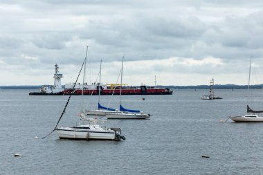 Perth Amboy, New Jersey - 1 Ekim 2024: Bir römorkör, Perth Amboy 'daki Arthur Kill' den bir mavnayı geçirdi. Ön planda Raritan Yat Kulübü 'nden yelkenliler görülüyor..