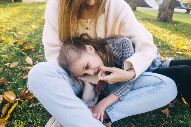 Anne ve kızı sonbahar parkında. Mutlu yüzler. Özel yaşam tarzı görüntü işleme. Çimenlerde ve sarı yapraklarda otururken. Mutlu anlar.