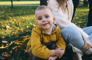 Anne ve oğlu sonbahar parkında. Mutlu yüzler. Yaşam tarzı görüntülerinin özel işlemleri. Çimenlerde ve sarı yapraklarda otururken. Mutlu anlar.