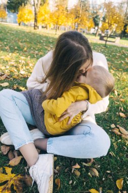 Anne ve oğlu sonbahar parkında. Mutlu yüzler. Yaşam tarzı görüntülerinin özel işlemleri. Çimenlerde ve sarı yapraklarda otururken. Mutlu anlar.