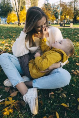Anne ve oğlu sonbahar parkında. Mutlu yüzler. Yaşam tarzı görüntülerinin özel işlemleri. Çimenlerde ve sarı yapraklarda otururken. Mutlu anlar.