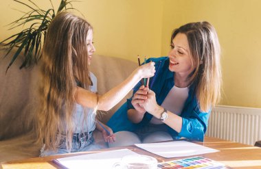 Anne ve kızı resim yapıyor. Resim öğretmeni suluboya boya, guaj tekniğini öğretir ve fırçayı doğru tutmayı öğretir. Mutlu çocukluk kavramı. Gülümseyen insanlar. Eğlence havası..