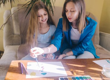 Anne ve kızı resim yapıyor. Resim öğretmeni suluboya boya, guaj tekniğini öğretir ve fırçayı doğru tutmayı öğretir. Mutlu çocukluk kavramı. Gülümseyen insanlar. Eğlence havası..
