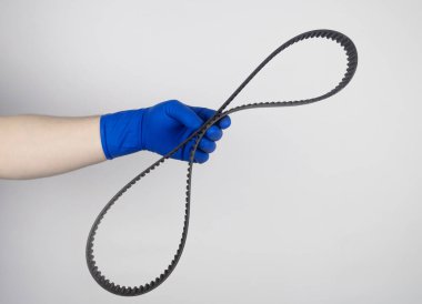 Zamanlama kayışı koptu. Arızalı bir motor şanzıman kayışı değiştiriliyor. Lastikte çatlaklar ve kırık kablolar riski. Yönetmeliğe göre ekipmanların değiştirilmesi. Mavi eldivenli tamirci.