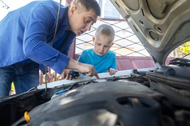 Baba oğluna motor bölümündeki soğutucuyu nerede dolduracağını gösteriyor. Arabanın soğutma sistemindeki antifrizi dolduruyorum. Motorun yakınındaki genişleme tankı. Kırmızı sıvı