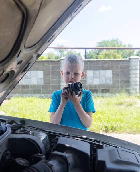 A mechanic dad teaches his son how to change the timing belt and car cooling pump at home. Child holds a pump in his hand. Maintenance of the car according to the regulations. New parts
