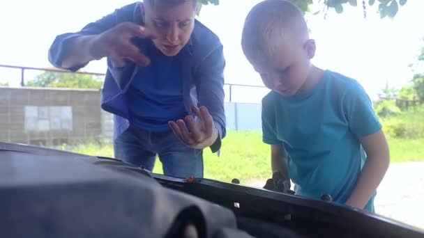 オイルレベルチェック 男は車のエンジンのオイルレベルを確認する方法を彼の息子を示しています 父は子供に内燃機関の仕組みを教える — ストック動画