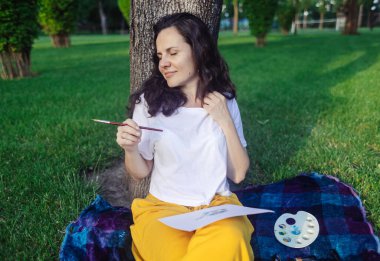 Sanat terapisi. Kadın parkta çizim yapıyor. Kız sırtı ağaca dönük oturur ve mesafeye bakar. Çizim yardımı ile sinir sisteminin yenilenmesi. Rahatlama ve meditasyon durumu kavramı