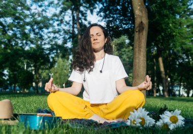 Parkta yalnız yoga. Kadın, Lotus pozisyonunda meditasyon yapmakla meşgul. Sinir sisteminin gevşemesi. Sinir sistemini boşaltmak için kişisel yardım. Dinginlik ve iyileşme