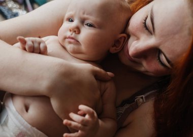 Genç anne çocuğun üzerine eğildi. Bir yavrunun sevgisi için el ele bir sembol. Şefkatli anne kavramı. Kızımla oyunlar. Doğal ebeveynlik ve çocuklara bakmak