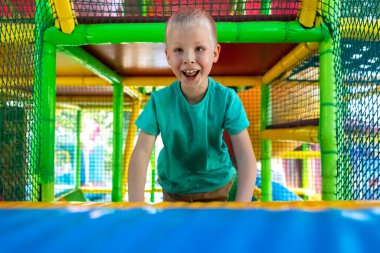 Oyun alanında oynayan sarışın bir çocuğun portresi. Çocuk labirenti. Yüze yakın çekim, mutluluk, eğlence ve dikkatsizlik duyguları. Tepe, labirent, trambolin. Çocuklar için güvenli bir cazibe