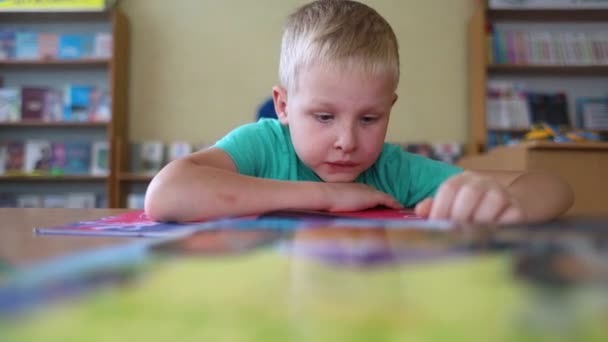 図書館にいる少年 7歳のウクライナ人男性が図書館のテーブルに座って本を読んでいる 通常の学習の概念 知識への渇望 新しいことを学びたいという願望 バックグラウンドと手紙 — ストック動画