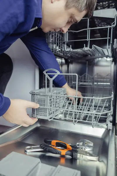 Dishwasher repair. A service center representative diagnoses and repairs a dishwashing machine at home. Specialist in working with home appliances. Call a technician to your home. Close-up