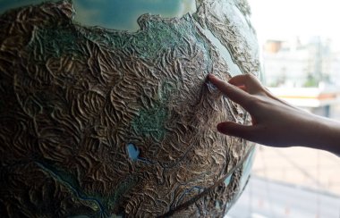 Çocuk dünyaya el ele tutuşuyor. Dünya gezegeninin büyük bir modelinin üzerinde bir çocuk eli. Çevreyi koruma, doğayı koruma ve parlak bir geleceğe inanma kavramı. Dünya ve çocuklar