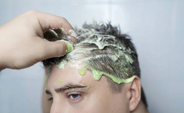 Man does head scrub. Dark-haired young man applies a scalp scrub to combat dandruff, oily scalp, alopecia. Problem skin causing hair problems. Close-up of self-massage and rubbing product into hair.