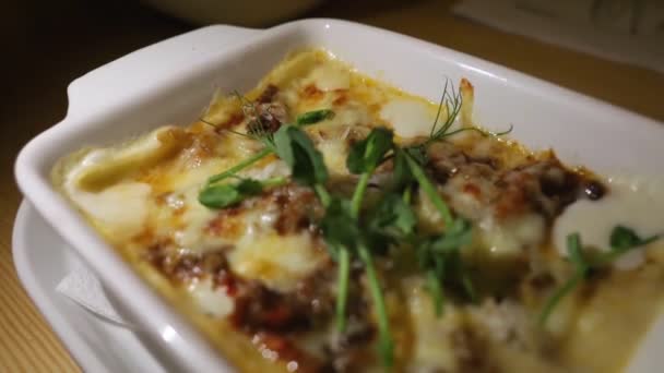 ラザニア 伝統的なイタリア料理 光源は動き 皿の金色のチーズの地殻に光の遊びの幻想を作り出します ホワイトプレートで焼いた料理のクローズアップ — ストック動画
