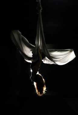 Sinek yogası. Siyah arka planda beyaz hamakta oturan kız hava akrobasisi gösteriyor. Jimnastik, sirk, kubbe altında. Işık ve gölge oyunu tiyatral bir performans hissi yaratır. Spor aktivitesi