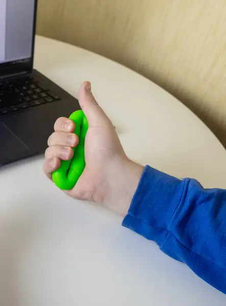Hand gripper. Man squeezes rubber expander while working on his laptop. Concept of combining useful activity with necessary work. Training hand and arm muscles. Multi-colored mini training apparatus