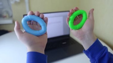 El sıkıştırıcı. Adam dizüstü bilgisayarı üzerinde çalışırken lastik genişleticiyi sıkıyor. Yararlı aktiviteyle gerekli işi birleştirme kavramı. Eğitimli el ve kol kasları. Çok renkli mini eğitim aparatı