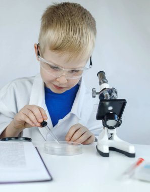 Çocuk kimyageri. Öğretmen görsel bir deney gösteriyor. Bir bilim danışmanı deneysel bir yaklaşım öğretir. Mikroskop, petri kabı, pipetler, kitaplar. Kimya veya fizik alanında pratik bir çalışma. Laboratuvar çalışması