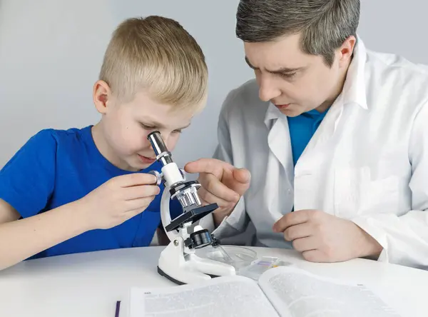 Child chemist. Teacher shows a visual experiment. A science mentor teaches an experimental approach. Microscope, petri dish, pipettes, books. Practical work in chemistry or physics. Laboratory work