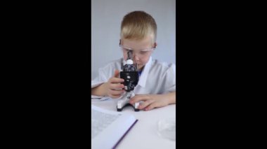 Çocuk kimyageri. Öğretmen görsel bir deney gösteriyor. Bir bilim danışmanı deneysel bir yaklaşım öğretir. Mikroskop, petri kabı, pipetler, kitaplar. Kimya veya fizik alanında pratik bir çalışma. Laboratuvar çalışması