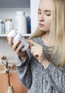 Kız, beslenme takviyeleri üzerine çalışıyor. Bir şişe vitamin kompleksinin talimatlarını okuyorum. Saç dökülmesi ve bağışıklığın zayıflaması için besin takviyesi. Reçetesiz ilaç kullanımı ve sağlığa zarar