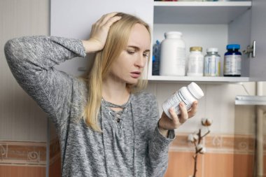 Kız, beslenme takviyeleri üzerine çalışıyor. Bir şişe vitamin kompleksinin talimatlarını okuyorum. Saç dökülmesi ve bağışıklığın zayıflaması için besin takviyesi. Reçetesiz ilaç kullanımı ve sağlığa zarar