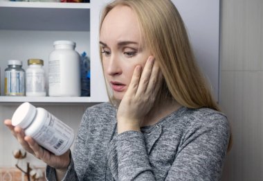 Kız, beslenme takviyeleri üzerine çalışıyor. Bir şişe vitamin kompleksinin talimatlarını okuyorum. Saç dökülmesi ve bağışıklığın zayıflaması için besin takviyesi. Reçetesiz ilaç kullanımı ve sağlığa zarar