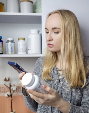 Kız, beslenme takviyeleri üzerine çalışıyor. Bir şişe vitamin kompleksinin talimatlarını okuyorum. Saç dökülmesi ve bağışıklığın zayıflaması için besin takviyesi. Reçetesiz ilaç kullanımı ve sağlığa zarar