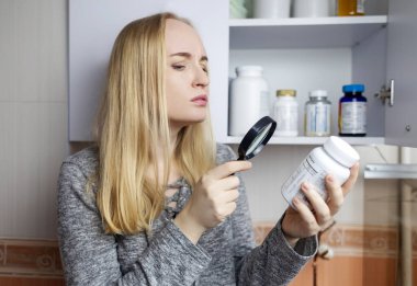 Kız, beslenme takviyeleri üzerine çalışıyor. Bir şişe vitamin kompleksinin talimatlarını okuyorum. Saç dökülmesi ve bağışıklığın zayıflaması için besin takviyesi. Reçetesiz ilaç kullanımı ve sağlığa zarar