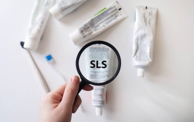 Dangerous toothpaste ingredient SLS, sodium laureth sulfate. Checking the composition of toothpaste with a magnifying glass against the background of many tubes clipart