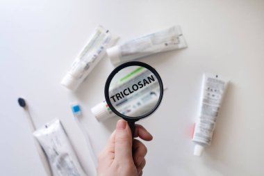 Dangerous toothpaste ingredient triclosan. Checking the composition of toothpaste with a magnifying glass against the background of many tubes clipart