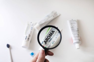 Dangerous toothpaste ingredient aroma. Checking the composition of toothpaste with a magnifying glass against the background of many tubes clipart