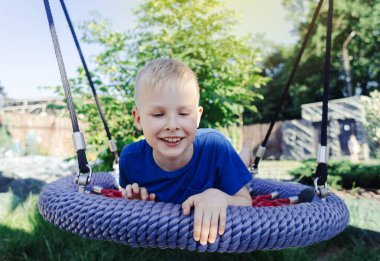 Mutlu sarı saçlı çocuk salıncakta ya da örümcek ağında geziyor. Parktaki çocuk parkında çekilmiş şirin bir portre. Yazın açık havada bir oyun.