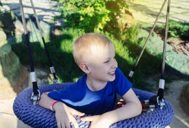 Mutlu sarı saçlı çocuk salıncakta ya da örümcek ağında geziyor. Parktaki çocuk parkında çekilmiş şirin bir portre. Yazın açık havada bir oyun.