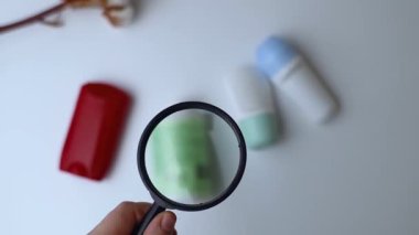 Deodorant içinde alüminyum. Tehlikeli bileşenler ve bakım kozmetik malzemeleri. Koltuk altlarının terlemekten korunması. Masada büyüteç altında duran top ve katı terletici maddeler var. 