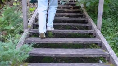 Akıllı telefonlu ve selfie çubuklu bir kız tahta merdivenlere tırmanıyor. Bacakların arkası. Bir kadın blogcu doğada güzel bir park olan botanik bahçesinde fotoğraf ve video çekiyor.. 