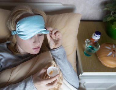 Bir kadın uyuyamaz ve bir kapsül melatoninle uyku hapı içmek ister. Jitlag veya uykusuzluk belirtileri. Biyolojik ritimlerin düzenlenmesi