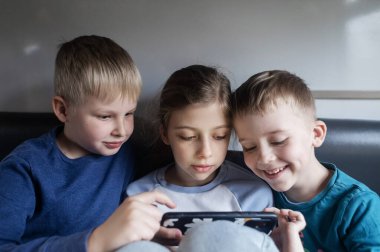 Children and the phone. Children's addiction to gadgets. Three children are traveling on a train and watching cartoons and playing games on a smartphone. clipart