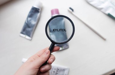 Xylitol in natural toothpaste. Magnifying glass is directed at a tube with a list of ingredients of a safe product. Safe toothpaste composition clipart