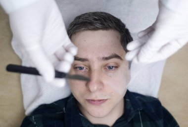 Bir dermatolog deri kazıması yaptırır ve deri iltihabı, mantar enfeksiyonu için testler yapar. Doktor randevusunda erkek bir hastanın yüzünü yakın plan çektir.