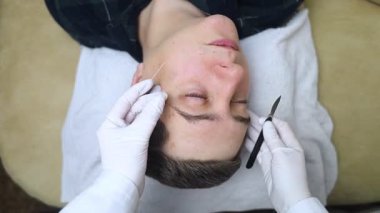 Bir dermatolog deri kazıması yaptırır ve deri iltihabı, mantar enfeksiyonu için testler yapar. Doktor randevusunda erkek bir hastanın yüzünü yakın plan çektir.