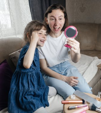 Kız, annesinin yüzüne makyaj yapar ve oynaşır. Bakıcı ebeveyn çocuğunun yüzünü boyamasına izin verir. Mutlu bir çocukluk. Sevgi dolu bir aile ve eğlence anlayışı. Küçük kız makyajını yapıyor.